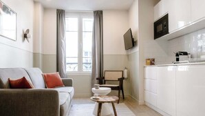Ein modernes Wohnzimmer mit einer Couch, einem kleinen runden Tisch und einer Küchenzeile mit weißen Schränken und einer Mikrowelle.