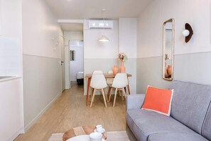 Ein modernes Wohnzimmer mit einem grauen Sofa, einem Holzesstisch mit Stühlen, einem kleinen Teppich und einem Spiegel an der Wand.