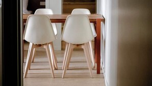 Een eetruimte met een houten tafel en witte stoelen, een hanglamp en een trap op de achtergrond.
