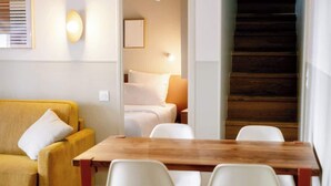 Een moderne kamer met een houten eettafel, witte stoelen, een geel bankje en een trap naar een verdieping erboven.