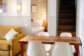 A modern room with a wooden dining table, white chairs, a yellow sofa, and a staircase leading to an upper floor. - Babylon Popincourt 23 (Paris)