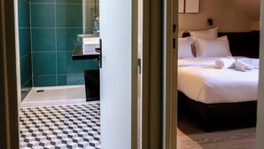 Hotellihuone, jossa on sänky, turkoosinvärinen kylpyhuone ja ruutukuviollinen lattia.