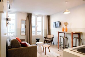 Ein modernes Wohnzimmer mit einer Couch, einem kleinen Tisch, einem Sessel und einer Küchenzeile mit Spüle und Barhocker.