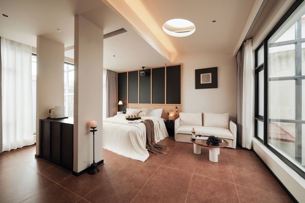 Una habitación de hotel moderna con cama, sofá, mesa de centro y un ventanal grande.