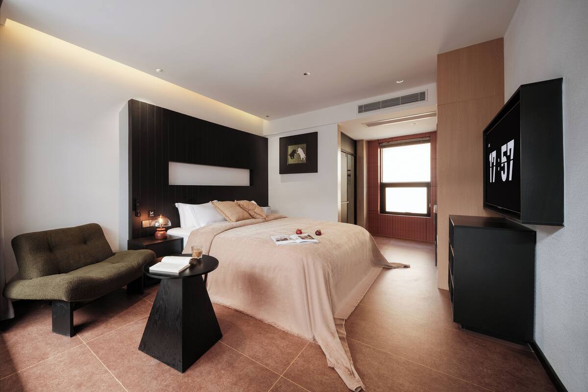 Una habitación de hotel moderna con una cama, un sofá, una mesita, un televisor y una puerta que da a otra habitación.