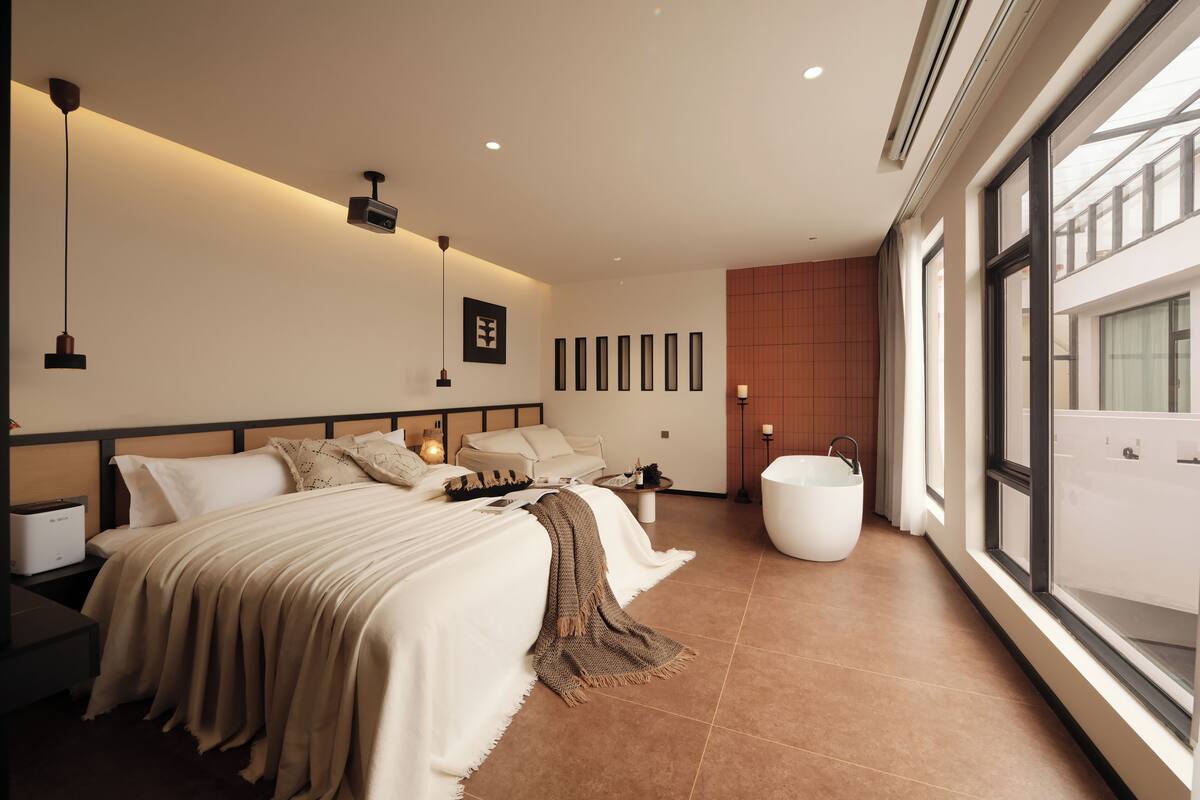 Un dormitorio moderno con una cama grande, mesitas de noche, un proyector empotrado en la pared y un amplio ventanal.