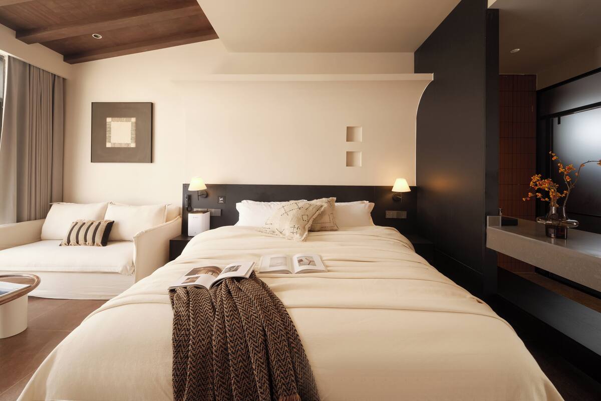 Una habitación de hotel moderna con una cama grande, un sofá, una mesita de noche y un televisor montado en la pared.