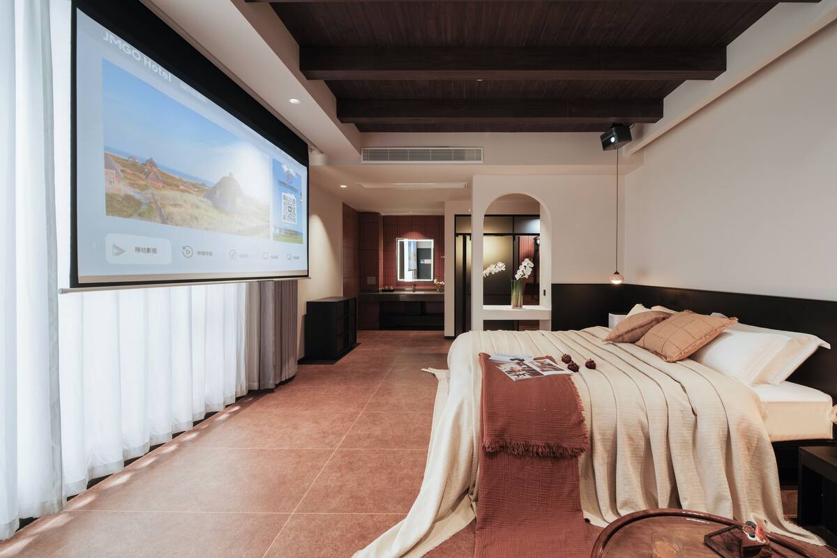 Habitación de hotel con cama, pantalla de televisión, techo de madera y vista al exterior.