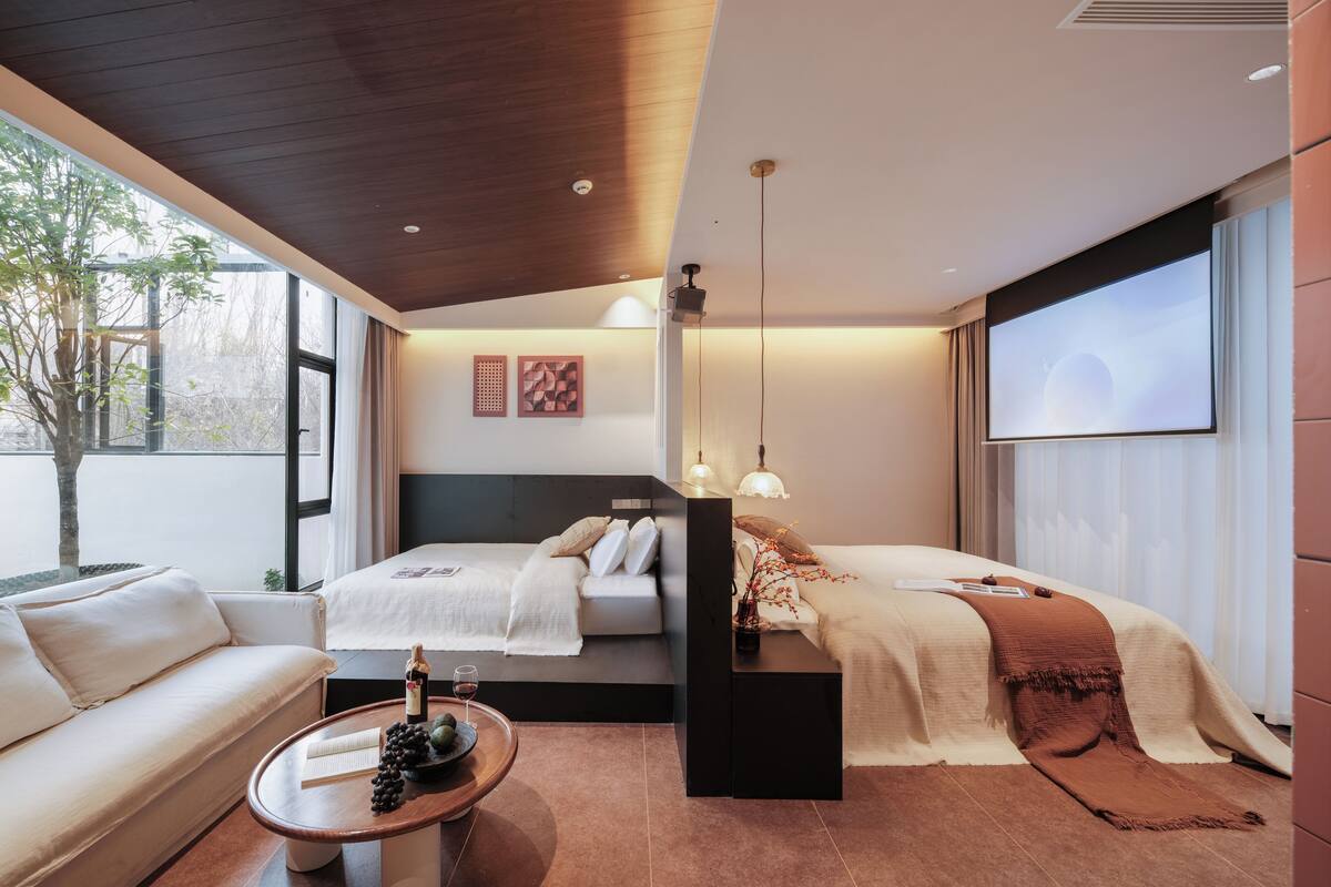 Una habitación de hotel moderna con una cama, un sofá, una mesa de centro con un libro y uvas, y un ventanal grande.