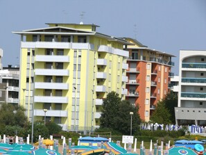 Ein mehrgeschossiges Gebäude mit Balkonen, einem Poolbereich mit Sonnenschirmen und blauem Himmel.
