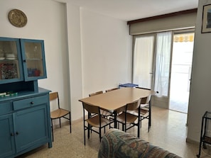 Ein Essbereich mit Tisch und Stühlen, eine blaue Kommode mit Glastüren und Blick durch ein Fenster mit Vorhängen.