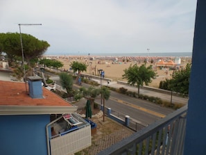 A balcony with a view of a beach, a street, and a building with a red roof. - Seafront flat with splendid views from the terrace (Bibione)