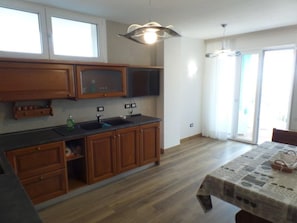 A kitchen with wooden cabinets, a black countertop, and a sink. There is a dining table with a tablecloth and a chair. - Seafront flat with splendid views from the terrace (Bibione)