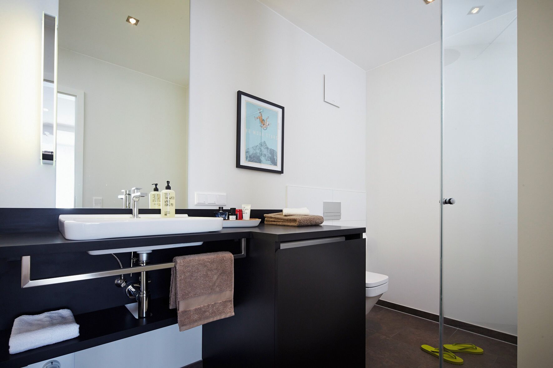 A modern bathroom with a large mirror, white sink, black countertop, and a framed picture on the wall.
