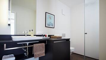 A modern bathroom with a large mirror, white sink, black countertop, and a framed picture on the wall.