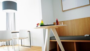 Moderni huone, jossa on puinen penkki, pyöreä pöytä, jonka päällä on pullo ja hedelmiä, sekä riippuvalaisin.