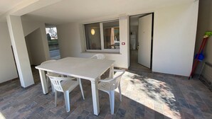 Una habitación con una mesa y sillas blancas, una ventana, una puerta y una mopa apoyada en la pared.