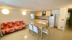 Un espacio habitable compacto con kitchenette, un comedor con mesa y sillas, y un sofá.