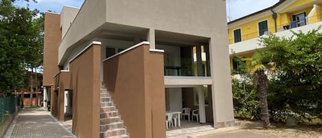 A modern building with a flat roof, a staircase leading to an upper level, and a patio area with outdoor seating.