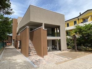 Ein modernes Gebäude mit Flachdach, einer Treppe zu einer oberen Ebene und einer Terrassenfläche mit Außenmöbeln.