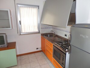 Eine Küche mit Gasherd, Backofen und einem Kühlschrank mit dem Aufdruck 'Rex'.