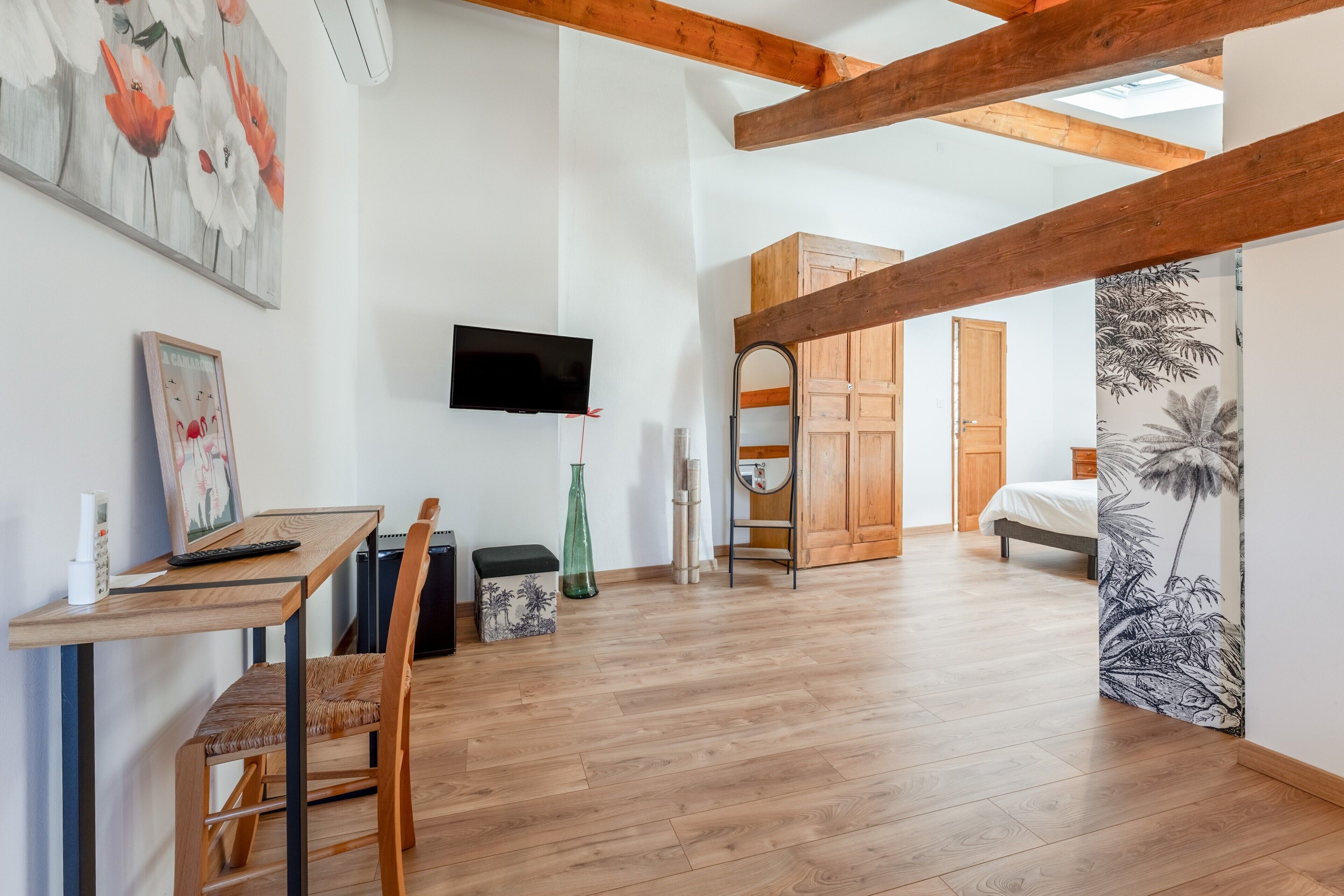 Een kamer met een houten vloer, een bureau met stoel, een aan de muur bevestigde televisie en een bed op de achtergrond.