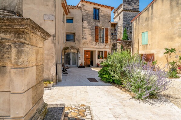 A narrow alleyway with stone buildings, a sign reading 'PLACE DU CHATEAU,' and a small courtyard with plants.