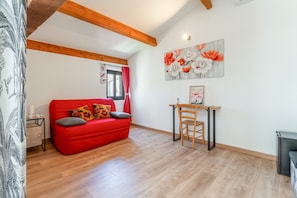 Une pièce avec un canapé rouge, un plancher en bois, une table à manger avec une chaise, et un tableau accroché au mur.