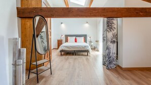 A bedroom with a bed, wooden beams, a skylight, a mirror, and a wall with a tropical plant mural. - Guest Room “Coquelicot” with Wi-Fi and Air Conditioning (Domazan)