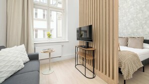 Una habitación de hotel moderna con sofá, televisión sobre un mueble, cama con cabecero estampado y ventana con cortinas.