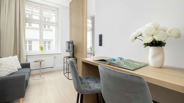 Una sala de estar moderna con un sofá, una mesa de comedor con sillas, una pequeña mesita auxiliar, un televisor y un jarrón con flores.