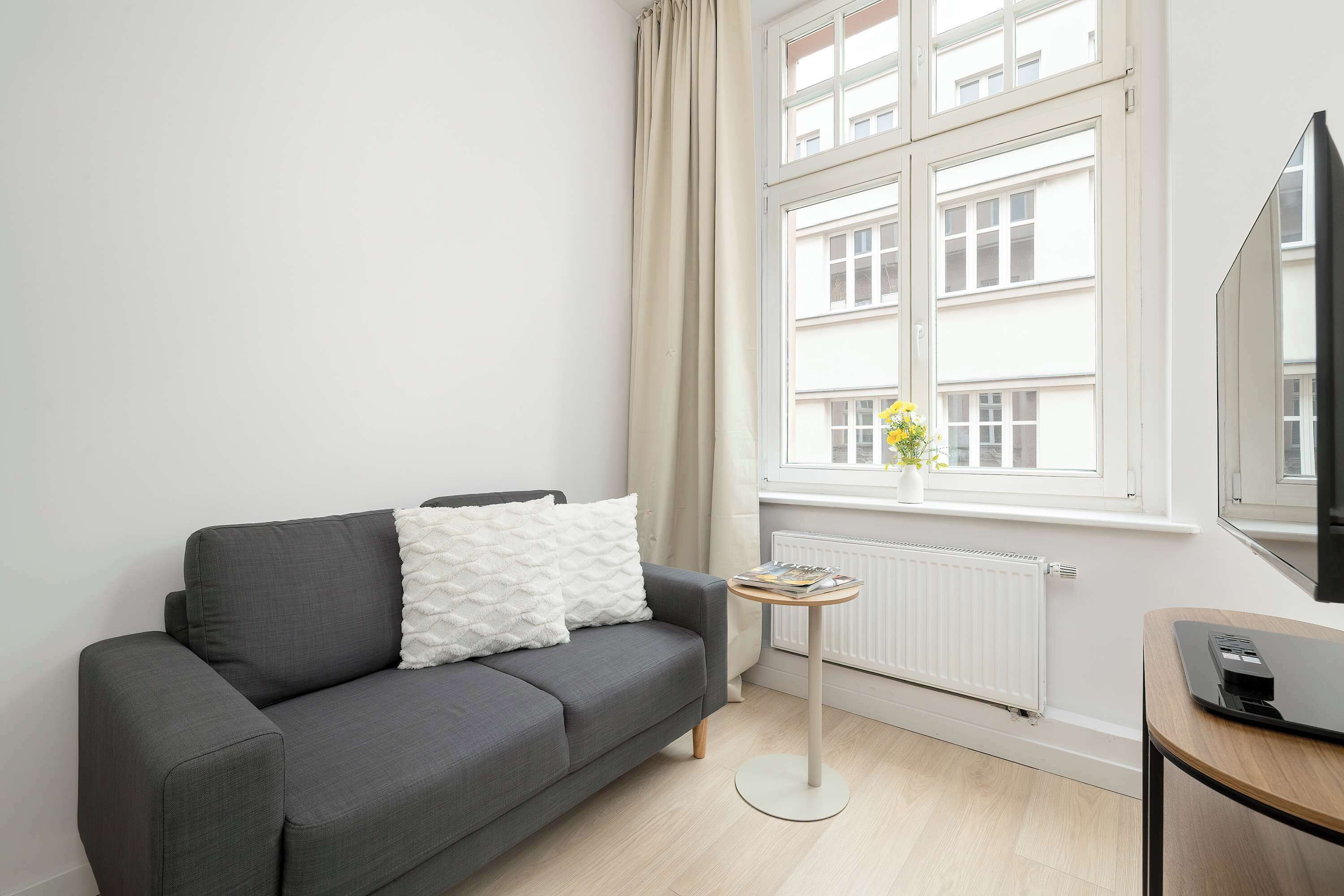 A modern living room with a grey sofa, a small round table, and a large window with a view of buildings.