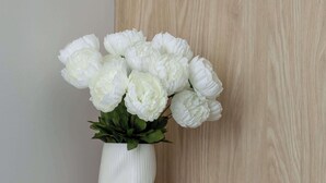 Un jarrón blanco con flores blancas sobre una mesa de madera junto a una silla.