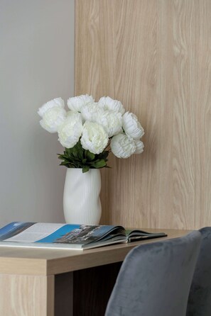 Eine weiße Vase mit weißen Blumen auf einem Holztisch neben einem Stuhl.