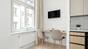 A modern kitchen with a built-in oven, a dining area with two chairs, a TV mounted on the wall, and a window with curtains. - Comfortable Studio in the Heart of Katowice | Remote Work Space (Katowice)