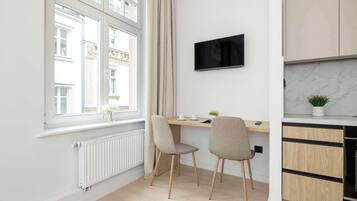 Una cocina moderna con horno empotrado, un área de comedor con dos sillas, un televisor montado en la pared y una ventana con cortinas.