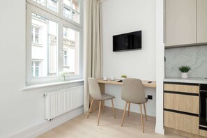 Eine moderne Küche mit Einbauofen, Essbereich mit zwei Stühlen, einem an der Wand befestigten Fernseher und einem Fenster mit Vorhängen.