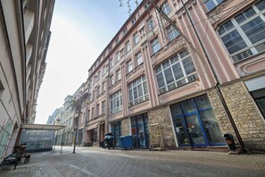 Straßenansicht mit einem Gebäude, großen Fenstern, einem Mülleimer und einem Wagen.