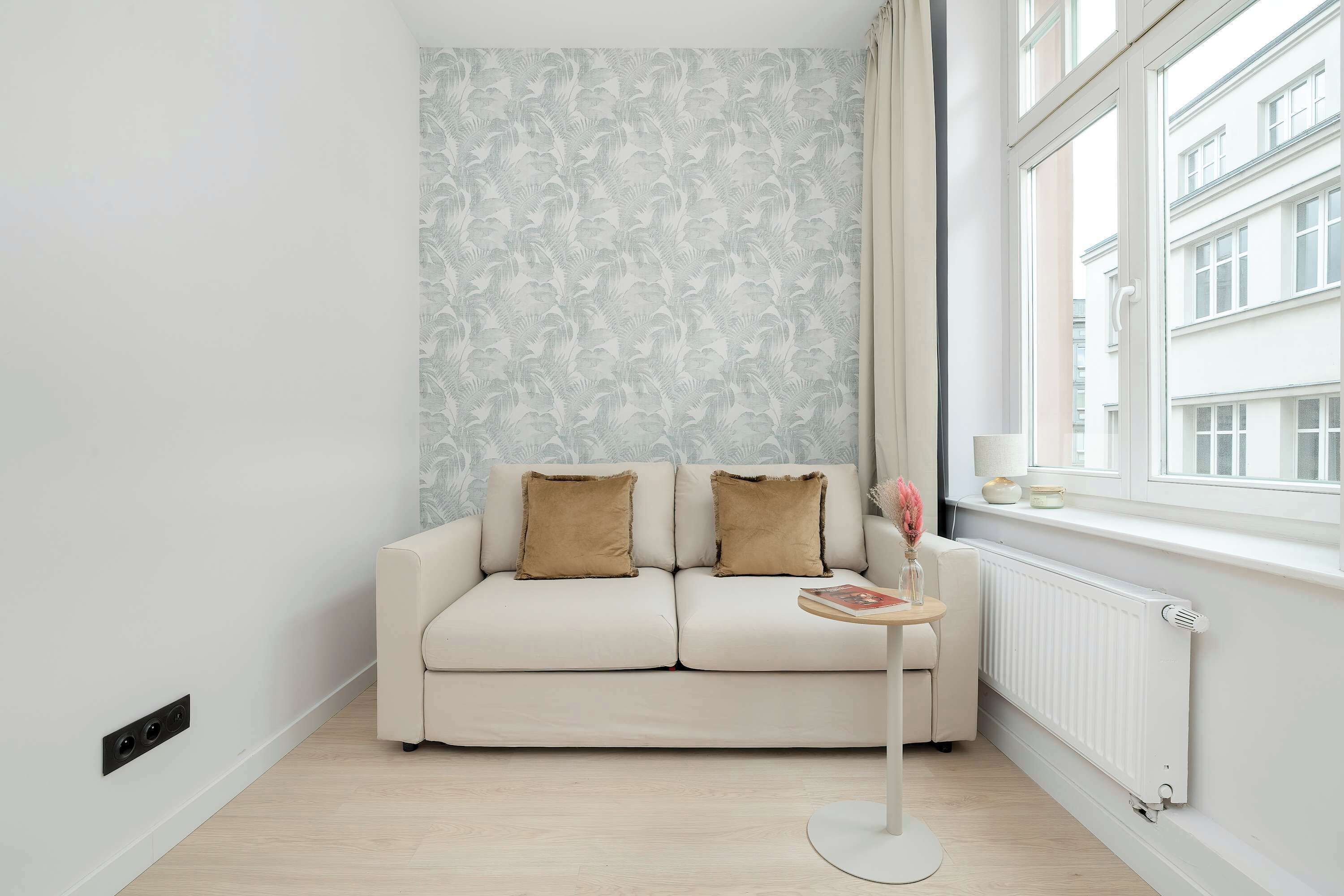 A modern living room with a sofa, a small round table, a radiator, and a window with a view of buildings.