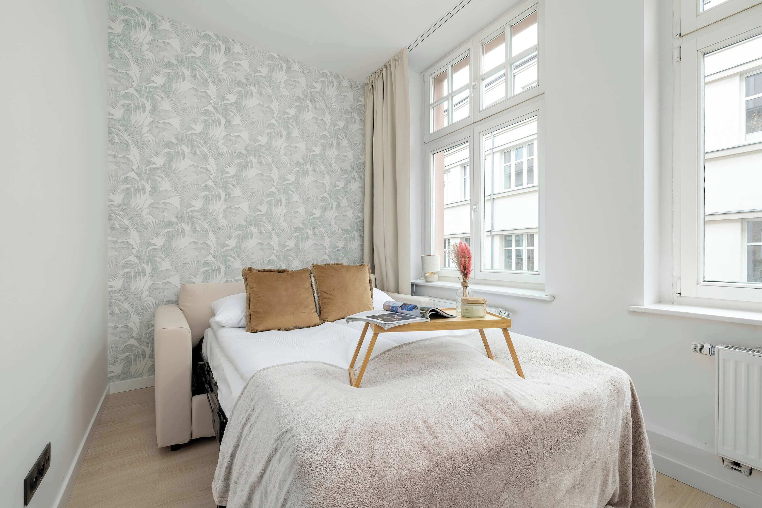 Ein Schlafzimmer mit einem Bett, einem Nachttisch mit einer Zeitschrift, einem Heizkörper und einem Fenster mit Vorhängen.
