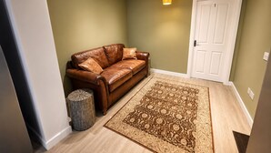 A room with a brown leather sofa, a patterned rug, a white door, and a small trash can. - House Sleeps 12 With Wifi (Bristol)