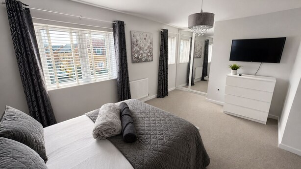 A bedroom with a bed, a dresser, a TV, and a window with curtains. - House Sleeps 12 With Wifi (Bristol)