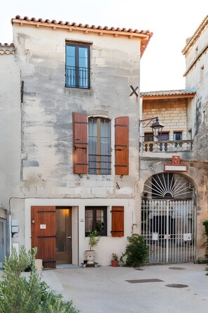 A stone building with a wooden door, a window with shutters, and a gate.
