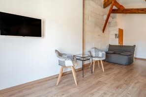 Een moderne woonkamer met een flatscreen televisie, twee gestreepten fauteuils, een glazen tafel, een grijze bank en houten vloer.