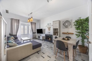 Ein modernes Wohnzimmer mit einer Couch, einem Fernseher, einem Kamin, einem Esstisch und einer großen Pflanze.
