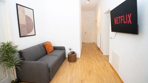 Ett modernt vardagsrum med en grå soffa, ett litet sidobord, en krukväxt och en väggmonterad tv som visar Netflix-logotypen.
