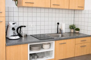 Eine Küche mit Spüle, Kaffeemaschine, Wasserkocher und einem Regal mit Tellern und Tassen.