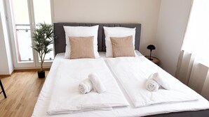 A neatly made bed with white linens and two pillows, a potted plant, and a bedside table with a lamp. - City apartment, incl. parking lot, near Europa-Park & Strasbourg & Black Forest (Offenburg)