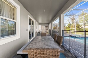 Eine überdachte Terrasse mit Pool, Korbmöbeln und Blick auf den Garten.