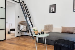A modern living room with a sofa, a round table, a chair, a ladder, and a framed picture on the wall.